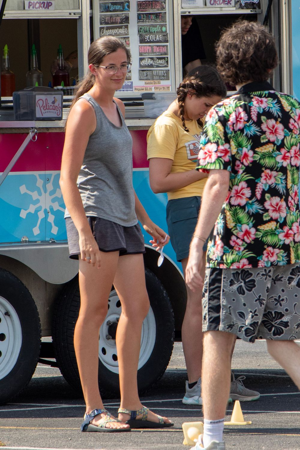 People order food from a blue and white ice cream truck with floral designs on a sunny day.