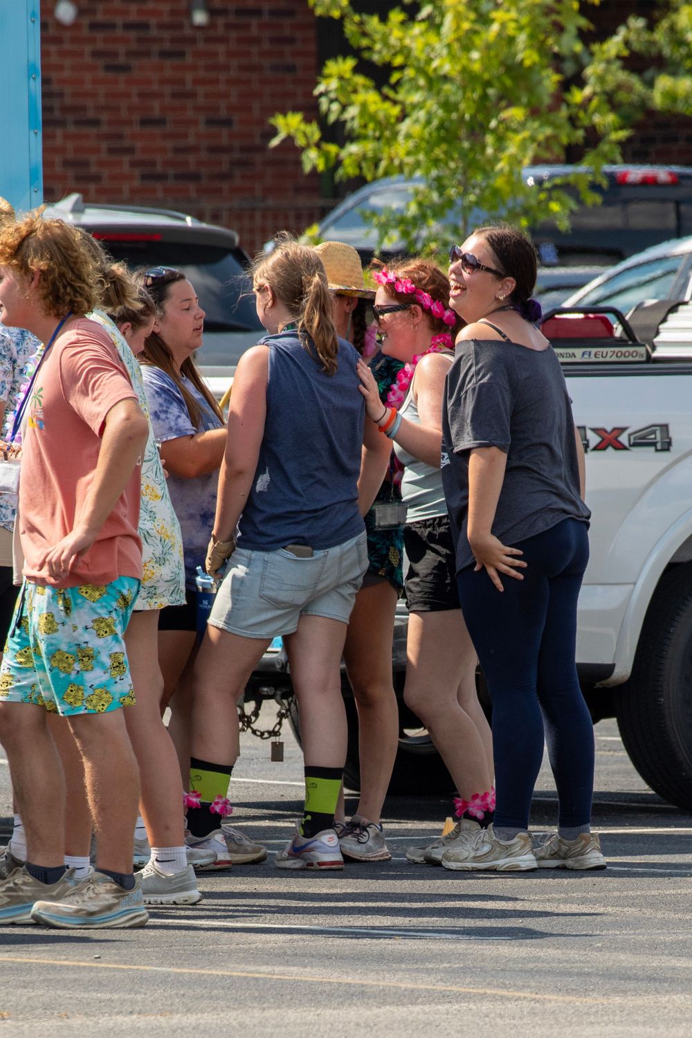 A line of people in shorts bend over in a parking lot during what appears to be an outdoor event or activity.