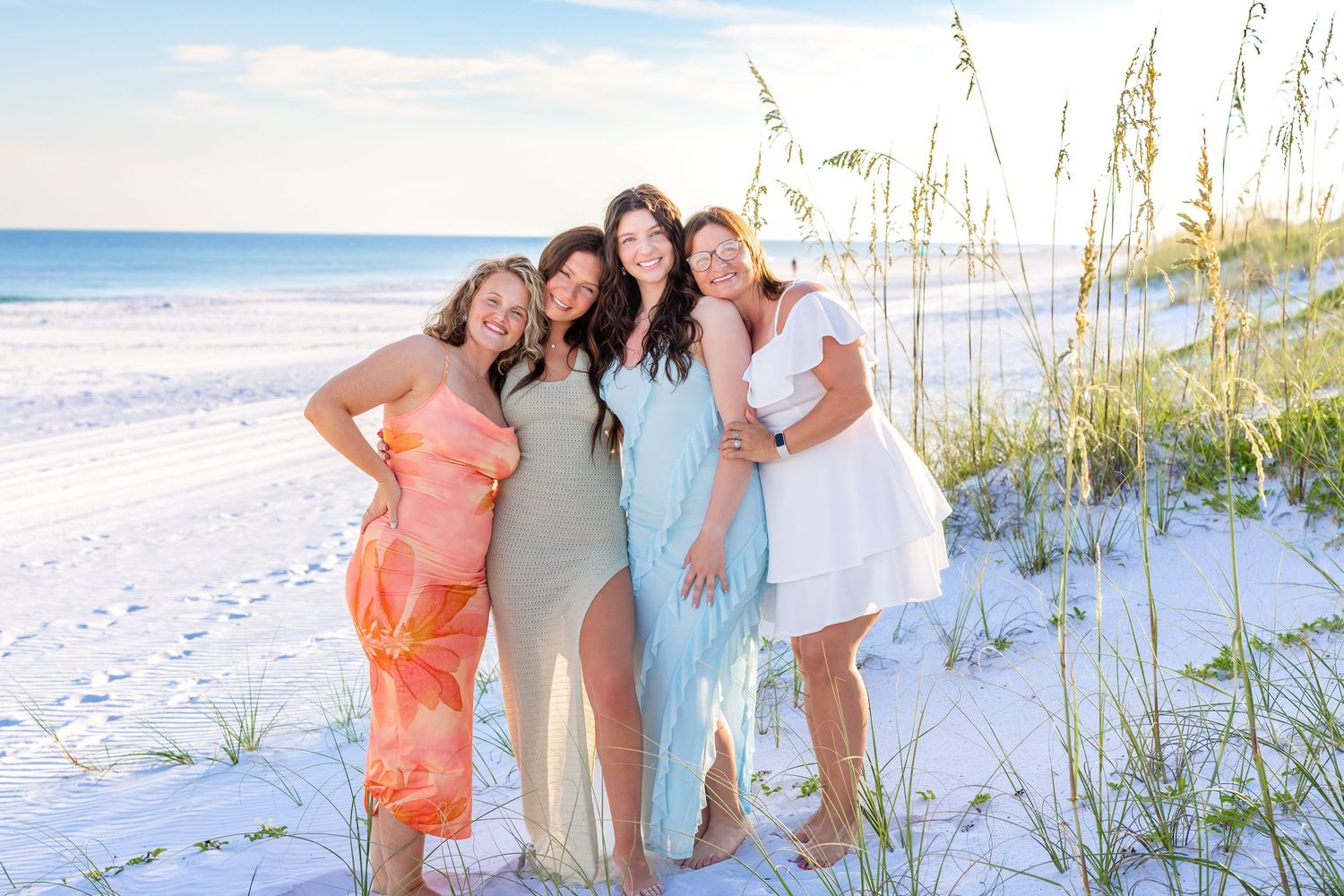 A group poses together on a white sandy beach at sunset with ocean waves and coastal buildings in the background.