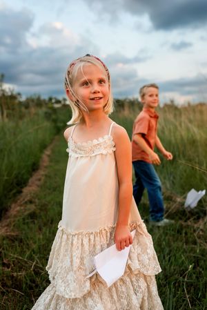 A sequence of candid moments showing a child in a white lace dress playing in a grassy field.