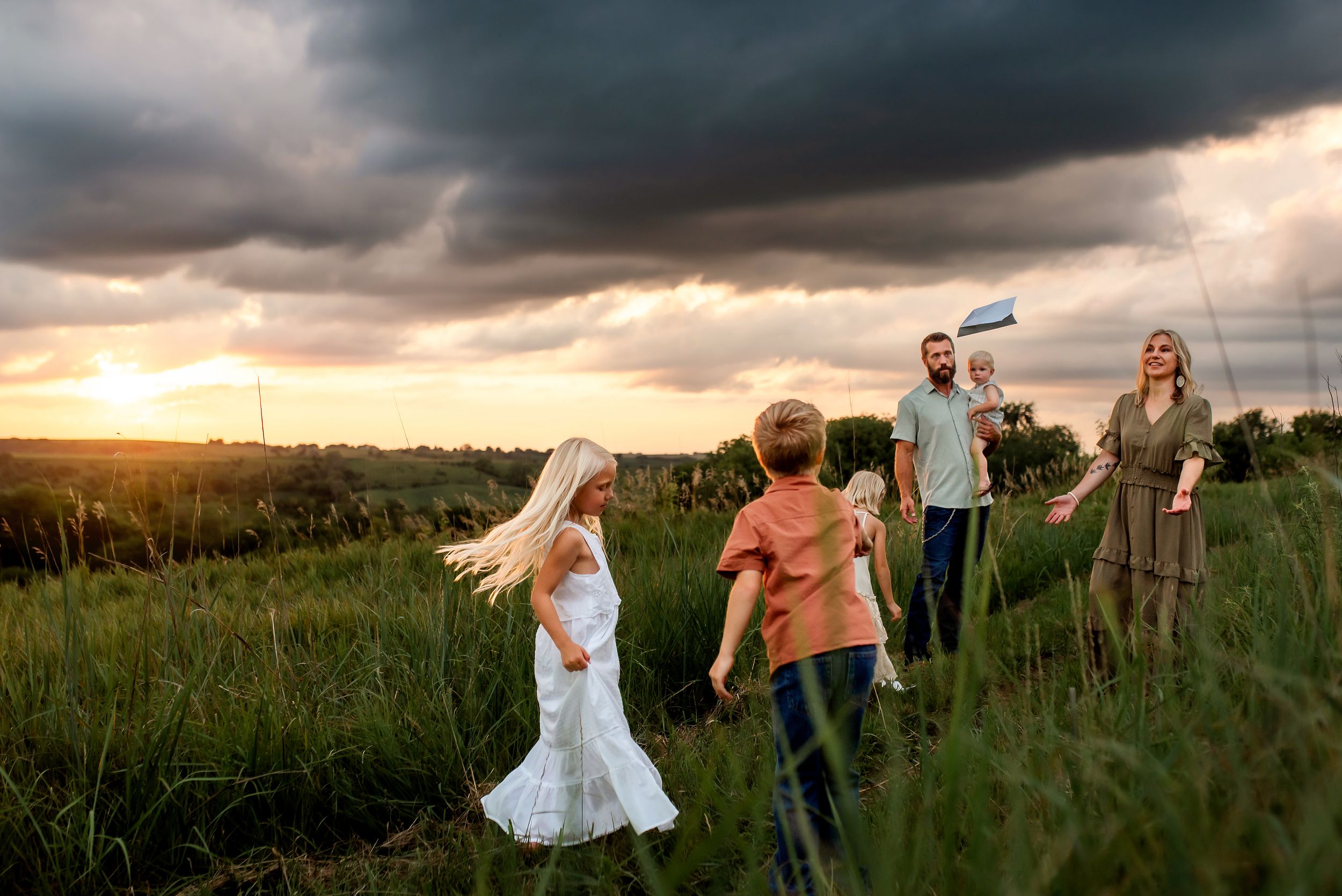 A group in a grassy field at sunset with a dramatic cloudy sky overhead.