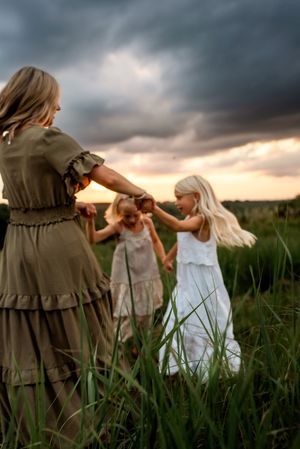 Dancing together in a grassy field under dramatic stormy clouds at sunset, creating a whimsical summer moment.