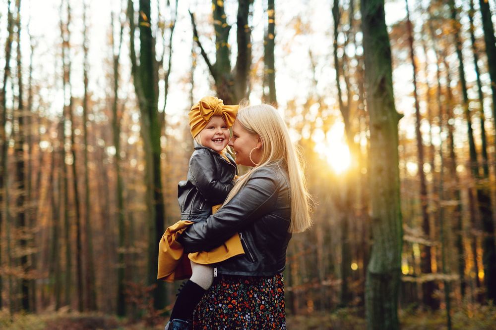 Two people embrace in a romantic moment at sunset in a wooded forest setting.