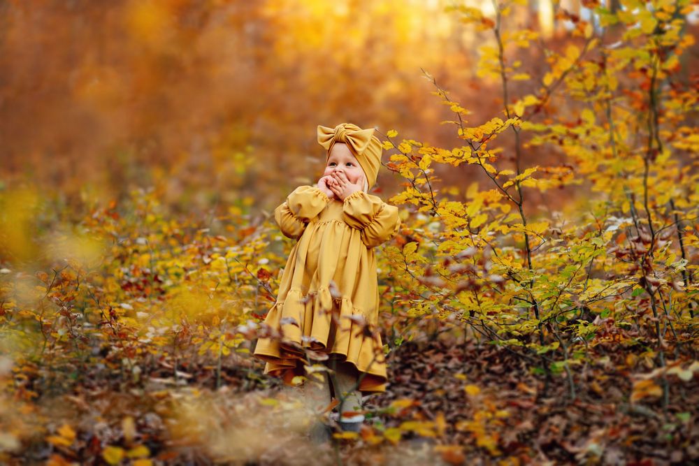 A figure in a yellow dress twirls playfully through autumn leaves in a golden-lit forest setting.