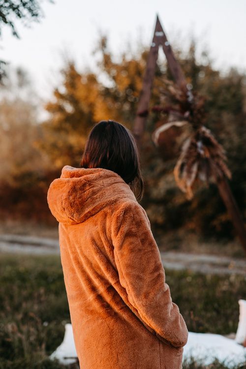 Someone wearing a cozy orange hoodie stands outdoors against an autumn backdrop with golden foliage.