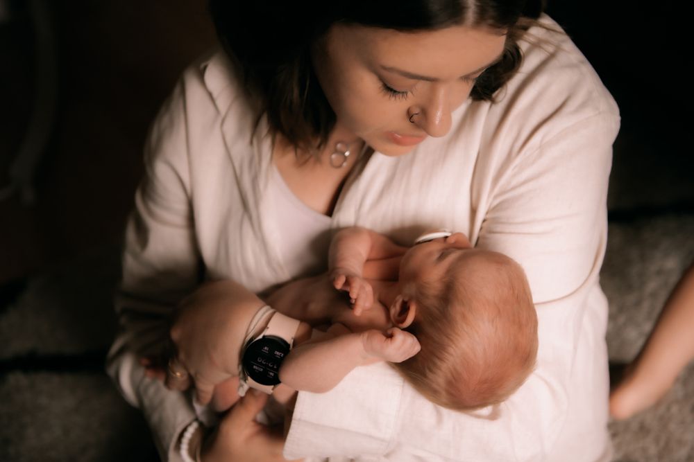 A mother in a soft cream sweater lovingly holds and gazes at her baby in a tender moment together.