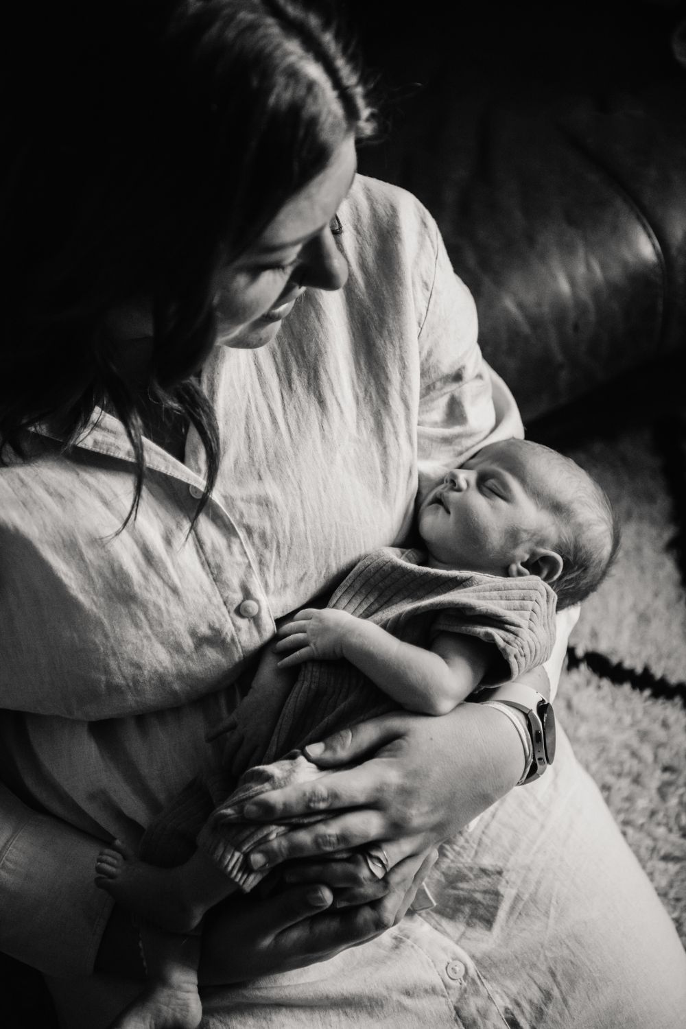 Black and white intimate portrait of a parent tenderly cradling a sleeping infant on a couch.
