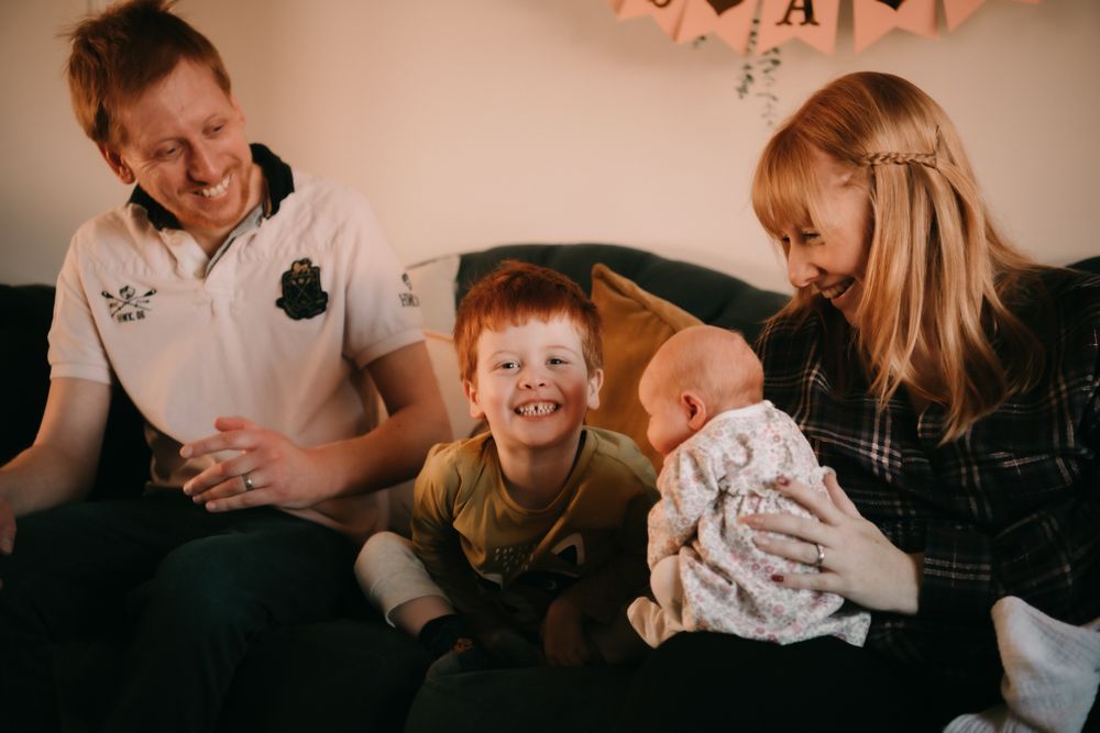 A family sharing a joyful moment together on a couch, laughing and interacting with each other.