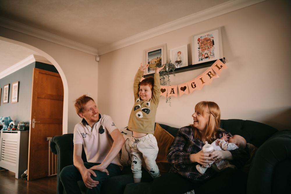 Family gathering in a living room with decorations and banner on the wall, relaxing together on a couch.
