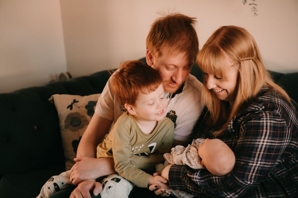 Family sharing a tender moment together while cuddling on a dark couch in warm lighting.