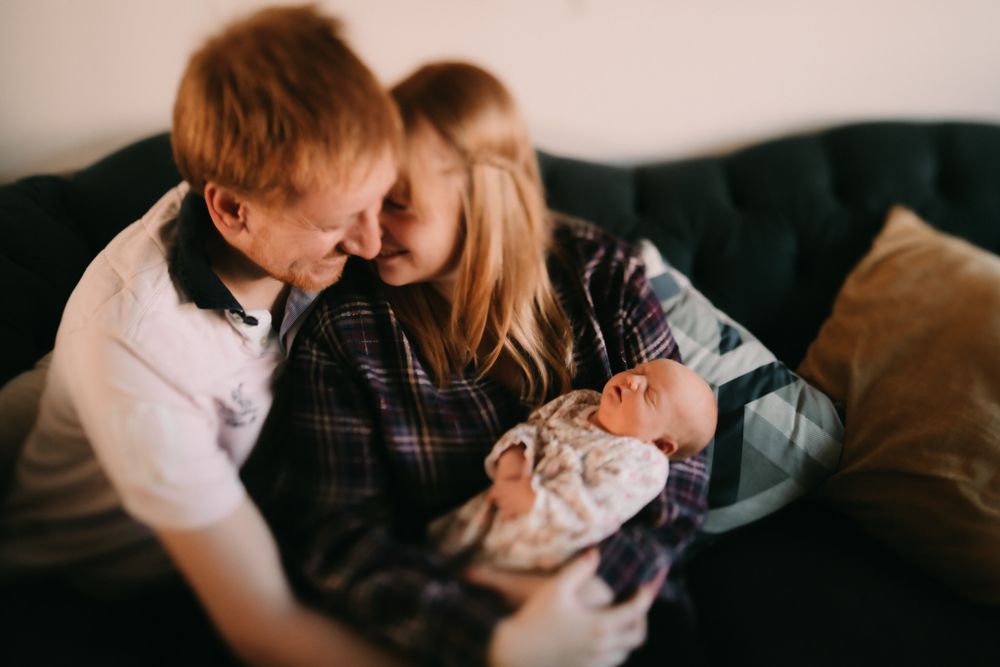 A cozy family moment on a dark sofa as they gaze at their newborn baby in a peaceful setting.