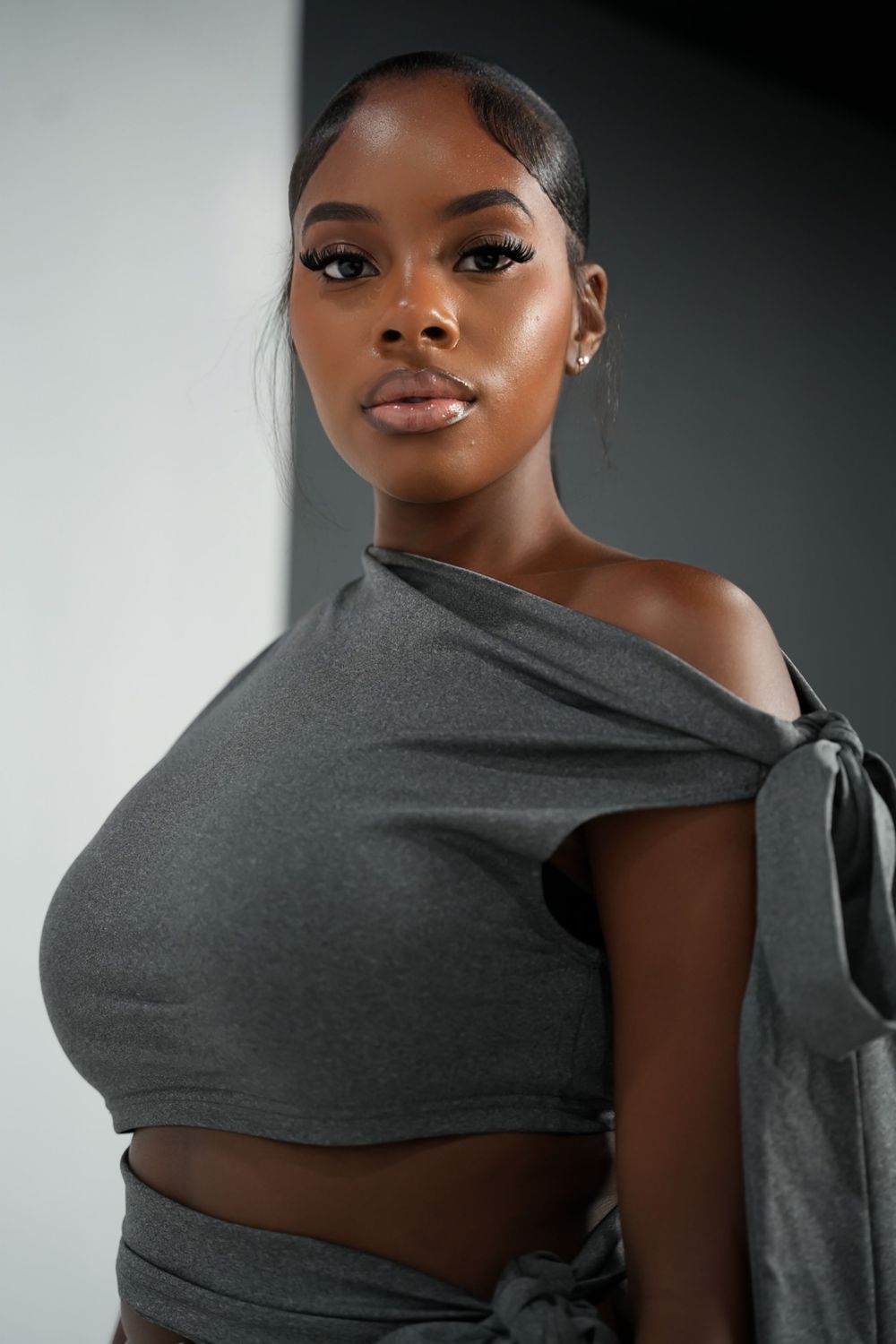 Studio portrait featuring an elegant grey one-shoulder top and dramatic lighting.