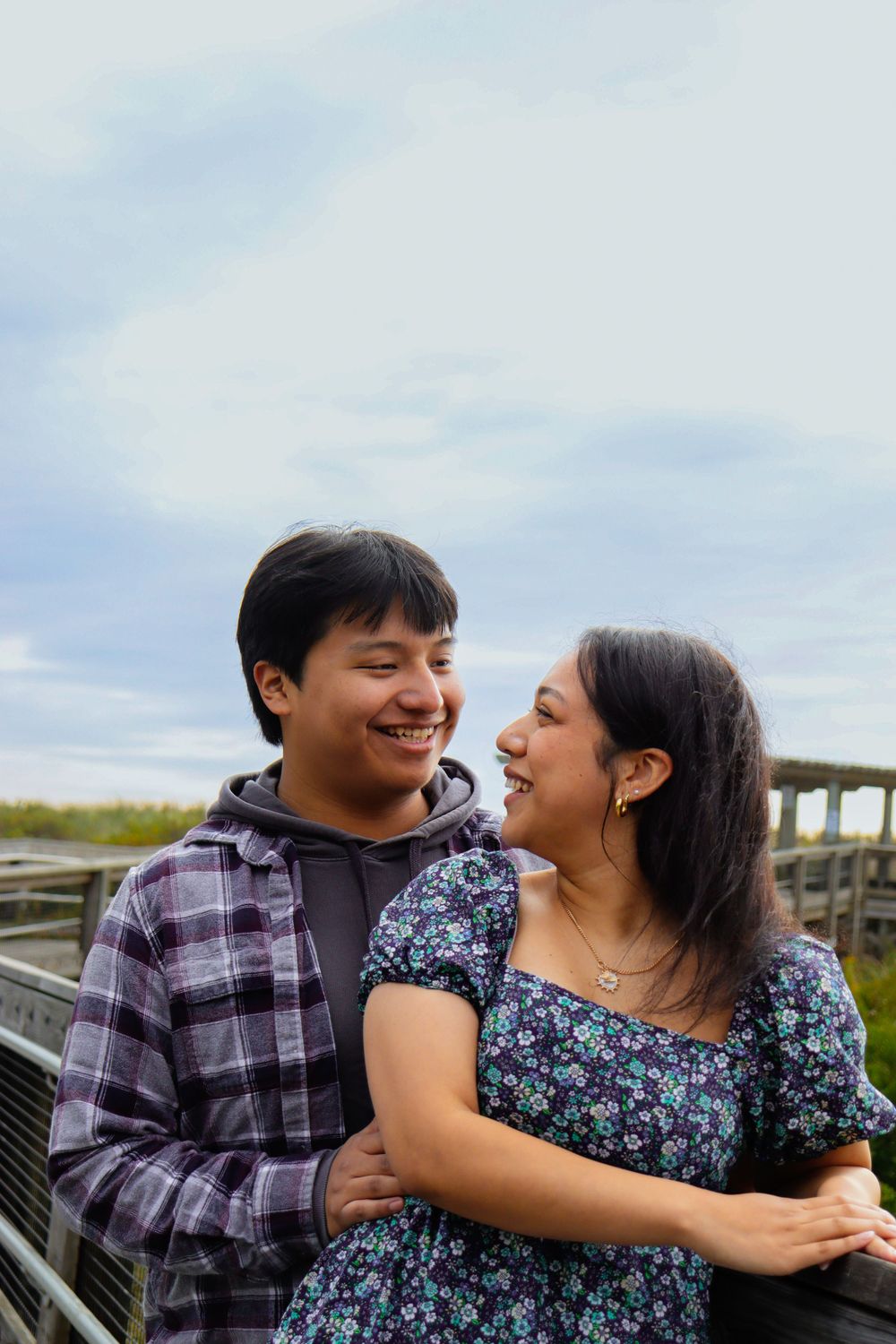 A couple shares a tender moment on a wooden boardwalk by the coast.