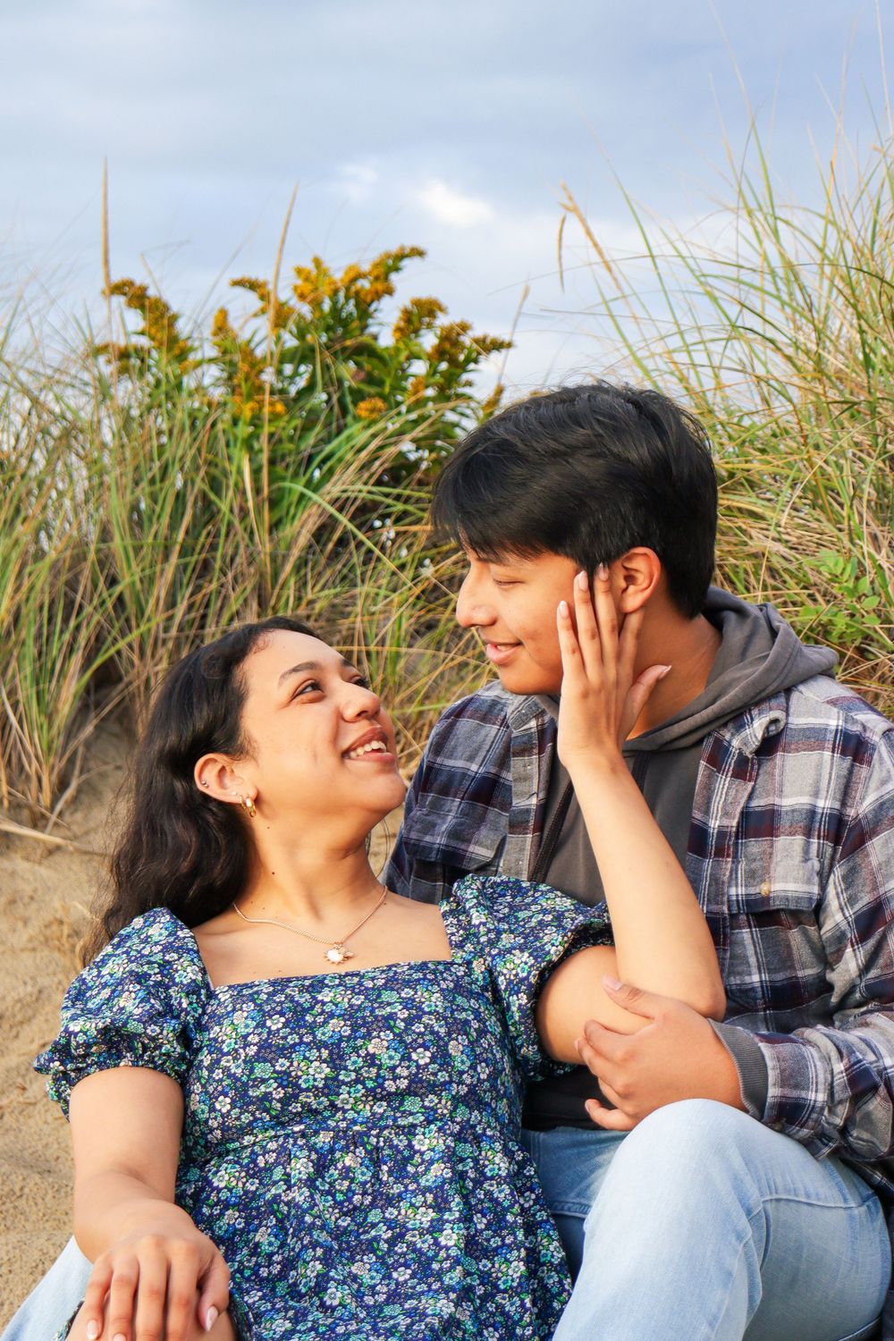 A couple relaxes in beach grass during a romantic coastal photoshoot.