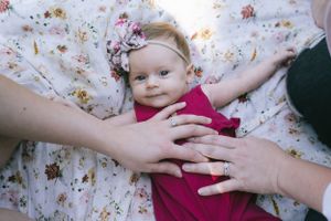 Gentle hands rest on a floral blanket with a small infant wearing red.