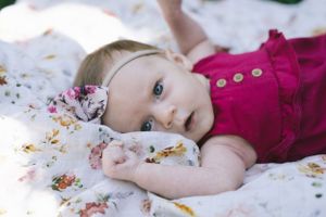 An infant in a pink dress rests on a floral patterned blanket.