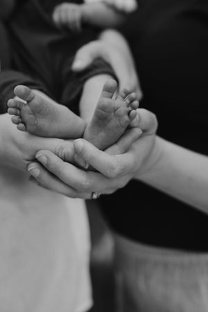 Black and white photo of tiny baby feet cradled in gentle hands.