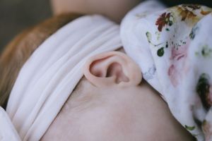 Baby's ear and profile wrapped in white blanket with floral pattern.