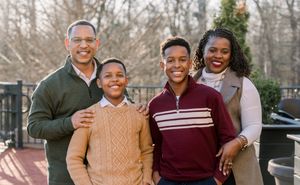 Outdoor family portrait with winter scenery and decorative greenery in background.
