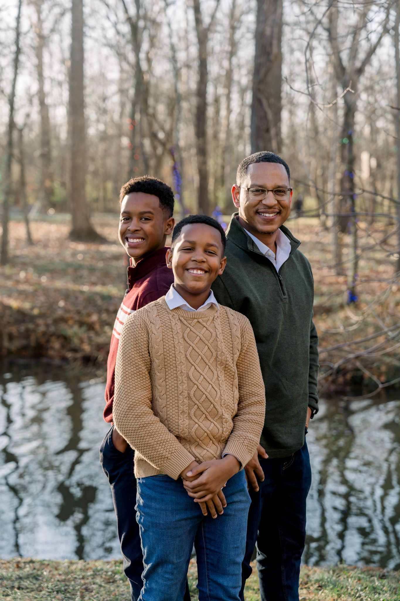Three people standing in line by pond with bare winter trees in background.
