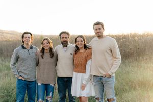 A group of five people in casual sweaters pose together in a golden field at sunset.