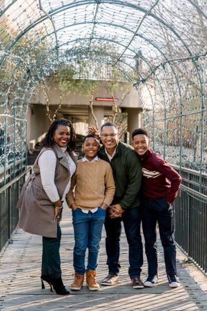 A family stands together smiling on a decorated bridge walkway with twinkling lights overhead.