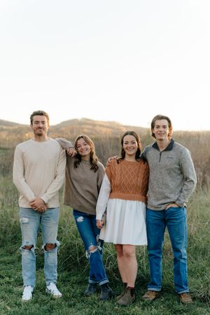 Four people in coordinating casual wear stand together in a field during golden hour.