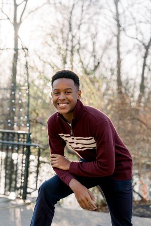 A person in a burgundy striped sweater poses outdoors with a bright smile.