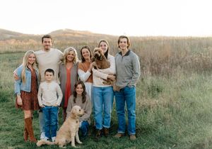 Family group gathers for casual outdoor photo with their pet dog in natural field setting.