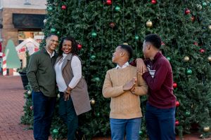 A group shares a candid moment of laughter by a festive Christmas tree outdoors.