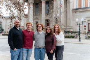 Group photo outdoors in front of historic building with decorative architecture in winter setting.