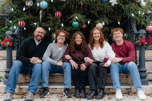 Group sitting on stone steps with decorated Christmas tree and ornaments in background.