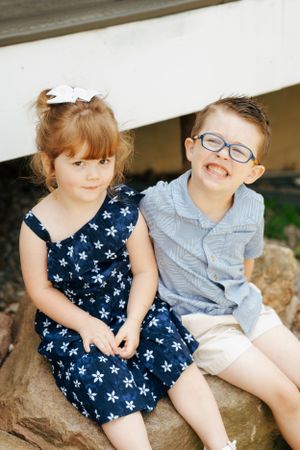 Two children sitting together on rocks wearing summer outfits with navy and blue patterns.