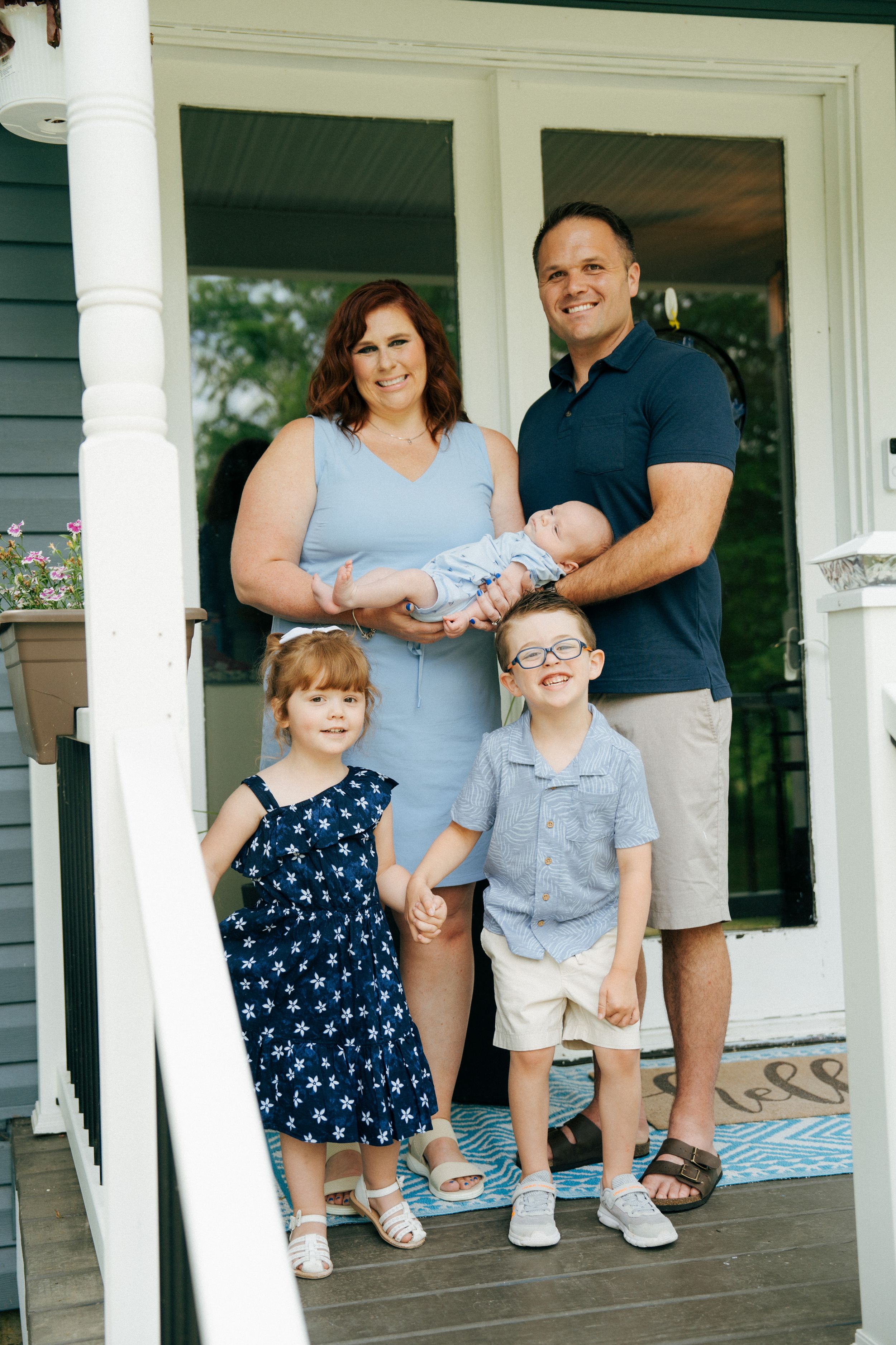 Family portrait on a front porch of a gray house with white trim.