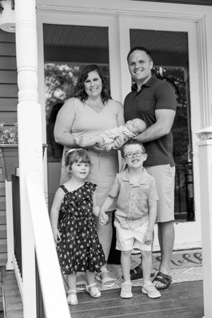 Black and white portrait of a family standing together on their front porch.