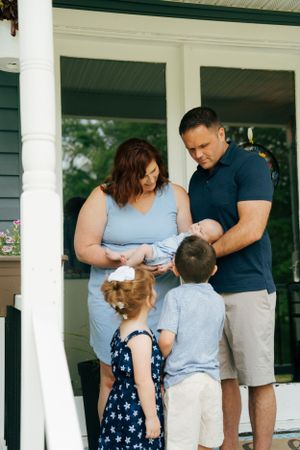 Family gathered on front porch of house with gray siding and white columns.