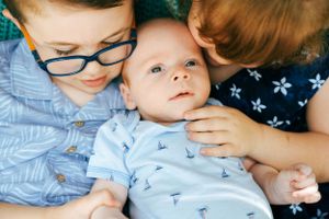 Three siblings sharing tender moment with youngest in blue outfit.