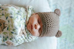 Baby wearing knit bear hat sleeping peacefully in floral swaddle.