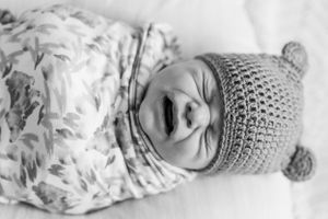 Black and white portrait of an infant in a knit bear beanie swaddled in floral fabric.