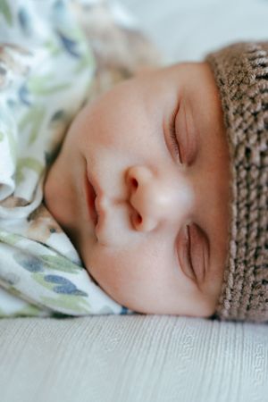 Dreaming baby in soft lighting wearing a brown knitted hat with bear ears.