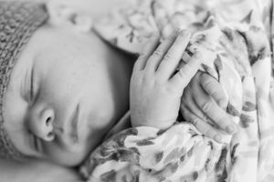 Black and white image of sleeping infant with tiny hand resting on floral swaddle.