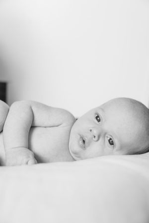 Black and white portrait of an alert infant lying on white bedding.