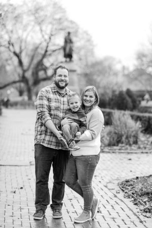 Black and white portrait of family standing on brick pathway.
