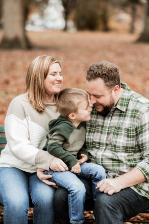 Family sharing joyful moment on park bench surrounded by autumn leaves.