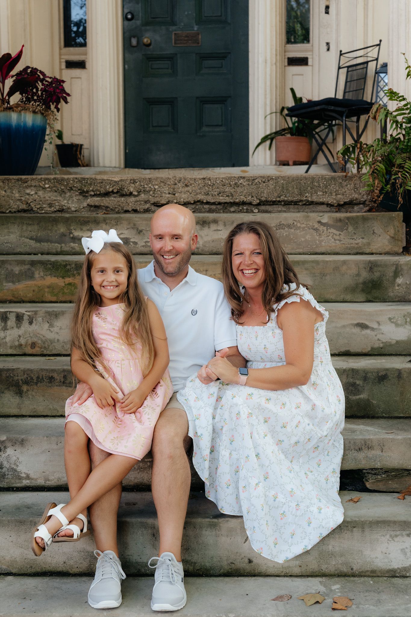 A family sits together on stone steps in front of a blue door in coordinated outfits.
