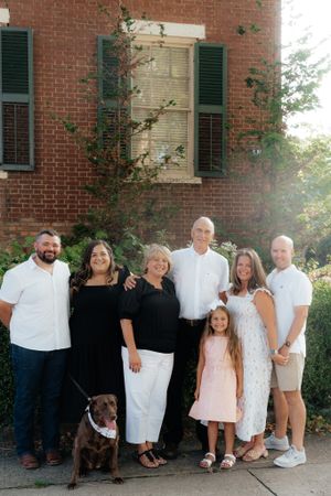 Extended family and their dog pose together against a brick building with green shutters.