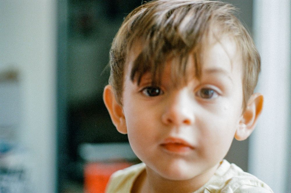 A young child in a beige shirt looking directly at the camera indoors.