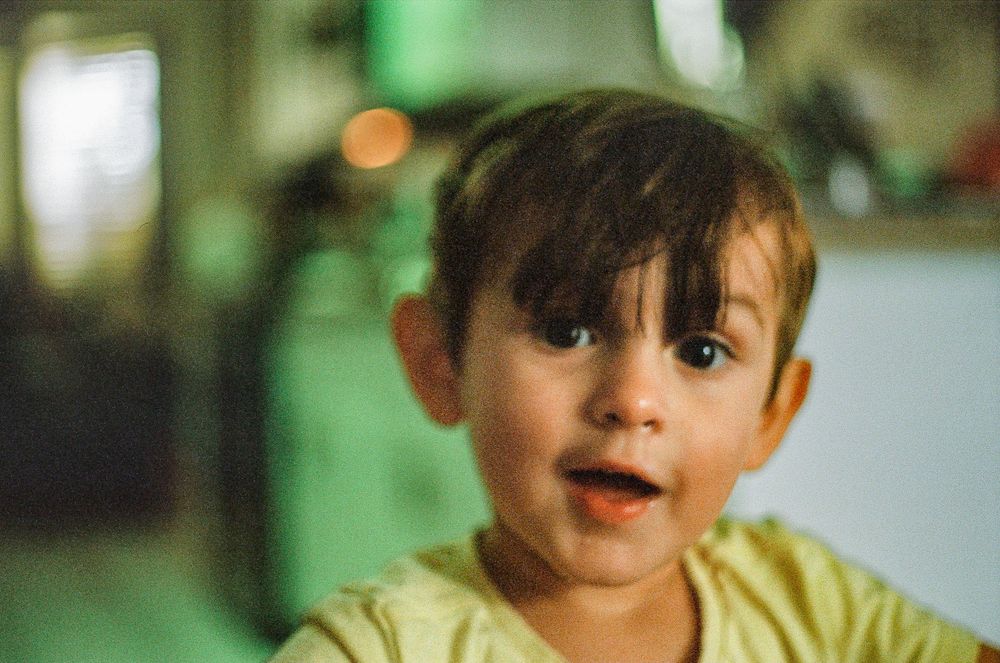 A child in a yellow shirt looking excited while indoors.