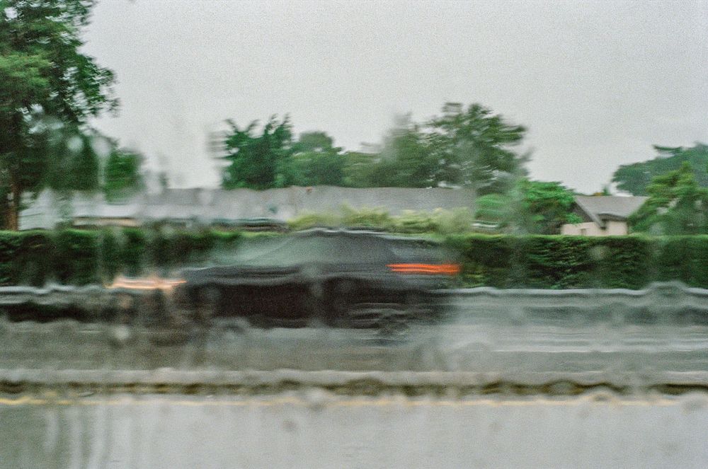 A blurry photo of a car driving in the rain on a wet road.