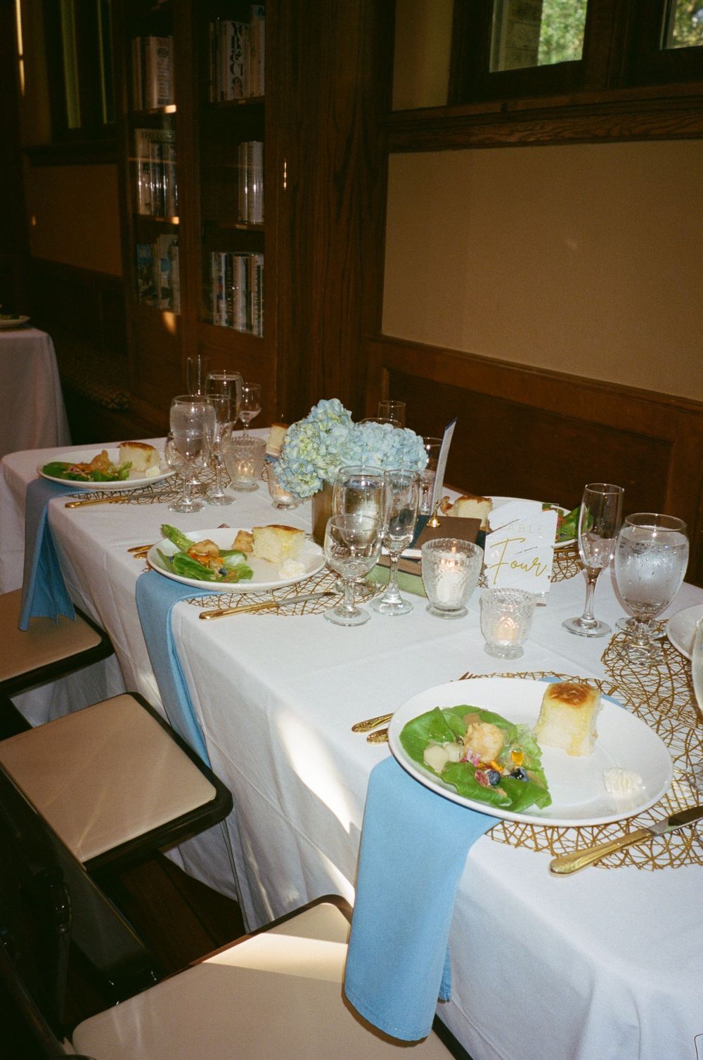 Formal place settings with salad courses and blue napkins on white tablecloth.